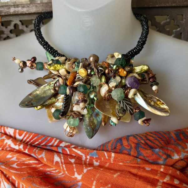 31. Designed by artist Jo Anne Brooks, this is a stunning statement piece made of copper combined with many exotic semiprecious stones and other found treasures. It features unlikely combinations of luxurious and found materials, contrasting colors & shapes, creating a playful contrast that is unified through texture! Jo Anne’s Story is a very unique and interesting one. “Polio, at the age of four left me without the use of both of my arms. While sitting on the floor, surrounded by mountains of supplies, I use my feet to guide and assist my left hand in creating jewelry. I combine copper, semi-precious stones and many other materials. This rare technique results in stunningly unique designs that are each as unusual as they way they were made! Jewelry should be fun, bring a smile to your face, and result in compliments from complete strangers! It should look as if it were made just for YOU and bring out the true colors of your life!”