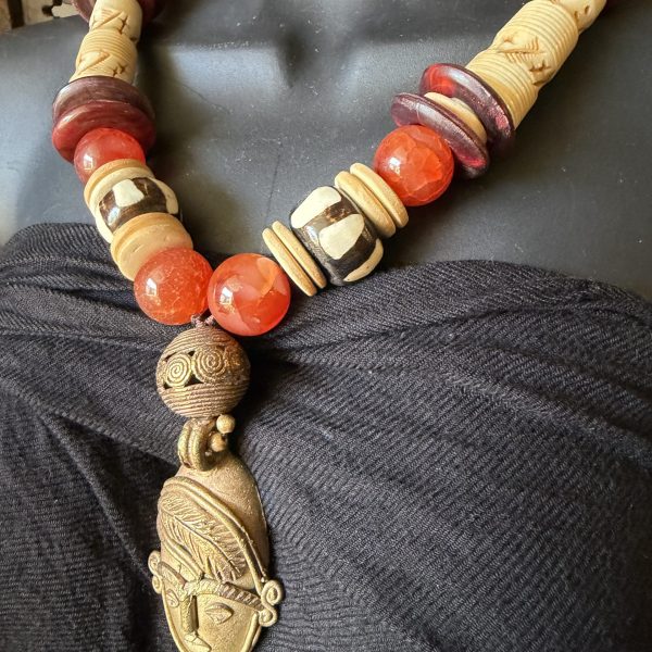 36. This stunning, exotic necklace by designer/artist Barbara Wright of Dallas, TX is a West African Pendant Necklace. This statement piece features wooden beads, vibrant red/orange carnelian beads, bovine beads, and hand dyed batik West-African beads. The detailed face pendant is crafted with brass and exudes an ethnic and regional charm that is both unique and eye-catching.