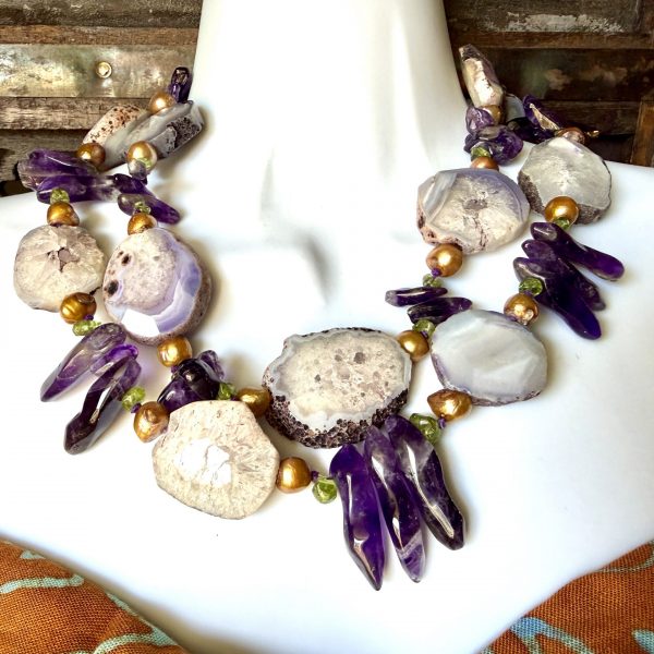 The Agate, Amethyst, Gilded Natural Pearls, and Peridot Necklace designed by artist Barbara Wright, is a stunning statement piece of handcrafted jewelry. The necklace features a beautiful main stone of Agate, with accents of Amethyst and Natural gold-gilded Pearls, beautifully contrasted with green peridot stones.