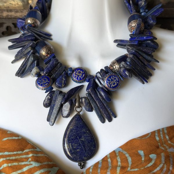 13. This STUNNING necklace features a stunning lapis lazuli pendant beads, and nuggets, set in silver, alongside blue Copal beads, and Chinese enamel metal beads. The deep blue color of the lapis lazuli and blue stones adds a touch of elegance and harmony to the piece. The unique style and materials used in this necklace make it a truly one-of-a-kind vintage piece designed by artist Barbara Wright of Dallas, TX is sure to be a conversation starter! Perfect for those who appreciate natural materials and traditional craftsmanship. Each bead is double-knotted by hand on silk thread. 18.5”