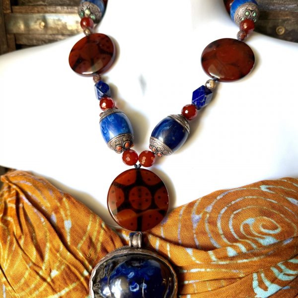 The Carved Blue Copal Pendant Necklace by artist Barbara Wright of Dallas, TX, features a beautiful pendant made from carved blue copal resin which depicts a rabbit. On the back of the pendant is an intricately created silver design of a rabbit as well. This pendant is complemented with beautiful turquoise, red copal (Tibet) , carnelian and lapis lazuli beads (Afghanistan,) measuring 19.5 inches in length. The design is inspired by several different world cultural traditions, showcasing intricate craftsmanship and a captivating bluish and orange color palette. The pendant is made with Tibetan silver metal and sourced materials from Tibet, adding a unique and authentic touch to the piece. The combination of gemstones and the artful design make it a stunning accessory for any jewelry lover looking for a one-of-a-kind piece. Each bead is double-knotted on silk thread!