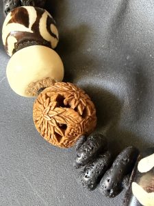 40. This stunning West African hand-carved wooden, bovine, and black lava rock beaded necklace designed by Barbara Wright of Dallas, TX, is a true masterpiece. The necklace features round-shaped beads made of black, brown, and white authentic materials ethically sourced from Kenya, showcasing a unique and ethnic regional style. This necklace features beautifully and intricately carved floral beads. The black and cream batik beads are crafted from bovine and the design is handmade, creating a visually striking piece that is sure to make a statement. Perfect for adding a touch of authentic African craftsmanship to any outfit, this necklace is a gorgeous and culturally-inspired accessory for any jewelry lover. Each bead is double-knotted by hand on silk thread!