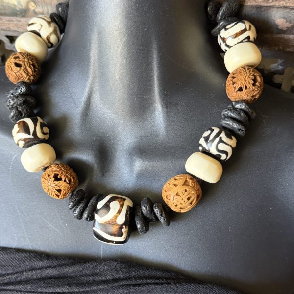 40. This stunning West African hand-carved wooden, bovine, and black lava rock beaded necklace designed by Barbara Wright of Dallas, TX, is a true masterpiece. The necklace features round-shaped beads made of black, brown, and white authentic materials ethically sourced from Kenya, showcasing a unique and ethnic regional style. This necklace features beautifully and intricately carved floral beads. The black and cream batik beads are crafted from bovine and the design is handmade, creating a visually striking piece that is sure to make a statement. Perfect for adding a touch of authentic African craftsmanship to any outfit, this necklace is a gorgeous and culturally-inspired accessory for any jewelry lover. Each bead is double-knotted by hand on silk thread!