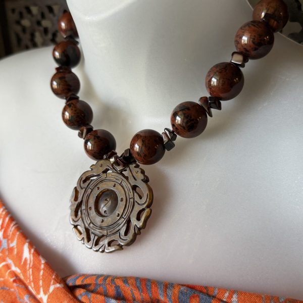 9. The Antique Brown Jade Dragon & Mahagony Obsidian Beaded Necklace designed by Barbara Wright of Dallas, TX, is a unique and handcrafted piece of jewelry. The necklace features brown jade as the main stone with beautiful mahogany obsidian as the secondary stones. It has a vintage style and is adorned with an intricate 2-dragon design and in the center is a rotatable yin yang, hand-carved making it a standout accessory for any outfit.