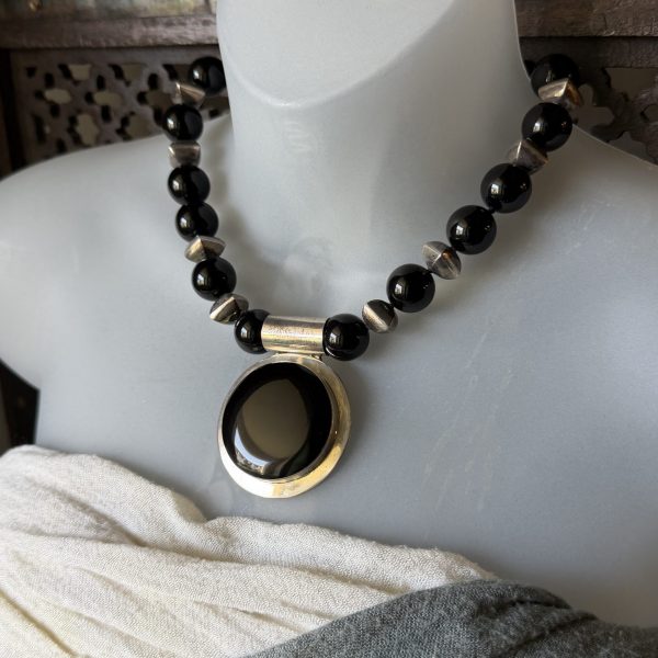 25. This Black Onyx Beaded Statement Necklace by designer Barbara Wright of Dallas Texas, features a striking oval pendant crafted from 925 sterling silver. The black Mexican onyx stones and unique silver beads add a touch of elegance and mystery to the piece, making it a versatile accessory that can elevate any outfit. The necklace's statement style and beaded design make it a bold and eye-catching addition to any jewelry collection. Each bead is double-knotted on silk thread!