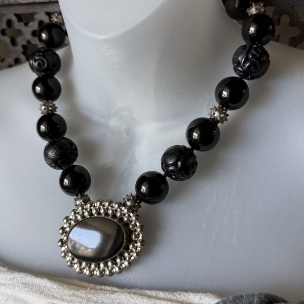 Designed by Barbara Wright of Dallas, Texas, this stunning Black Onyx Statement Necklace showcases a bold oval pendant set in genuine 925 sterling silver. Rich black Mexican onyx stones are paired with distinctive silver beads, creating a sophisticated piece with an elegant, slightly mysterious allure. The hand-knotted beaded design adds both beauty and craftsmanship, with every bead individually double-knotted on silk thread for durability and a luxurious finish. Striking yet versatile, this necklace makes a timeless statement whether dressed up or worn with everyday style.