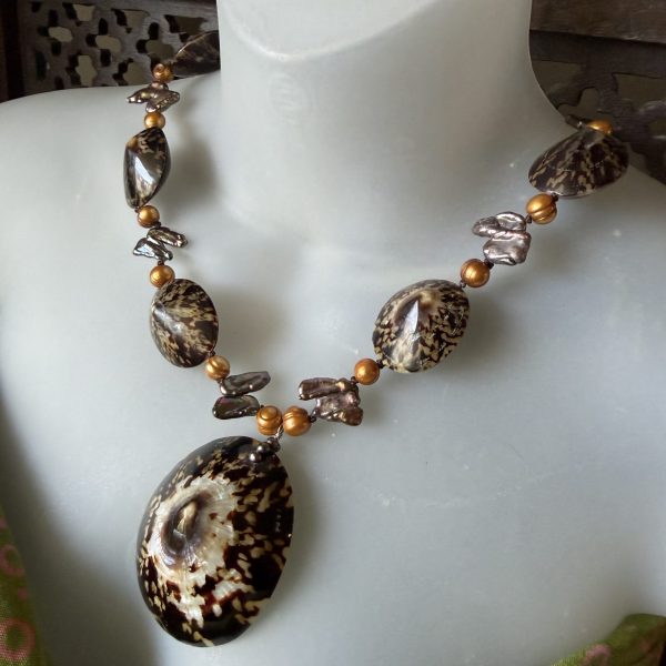 This Limpet Shell necklace, designed by artist Barbara Wright of Dallas, TX, features a unique combination of natural shells, gold gilded pearls and fresh water pearl beads, creating a luxurious and sophisticated accessory. The 20.5" necklace showcases a pendant style with a beautiful brown and iridescent light color and a nature-inspired theme. The limpet shell adds a touch of natural elegance to the piece, making it a perfect statement for any outfit- for a mermaid!
