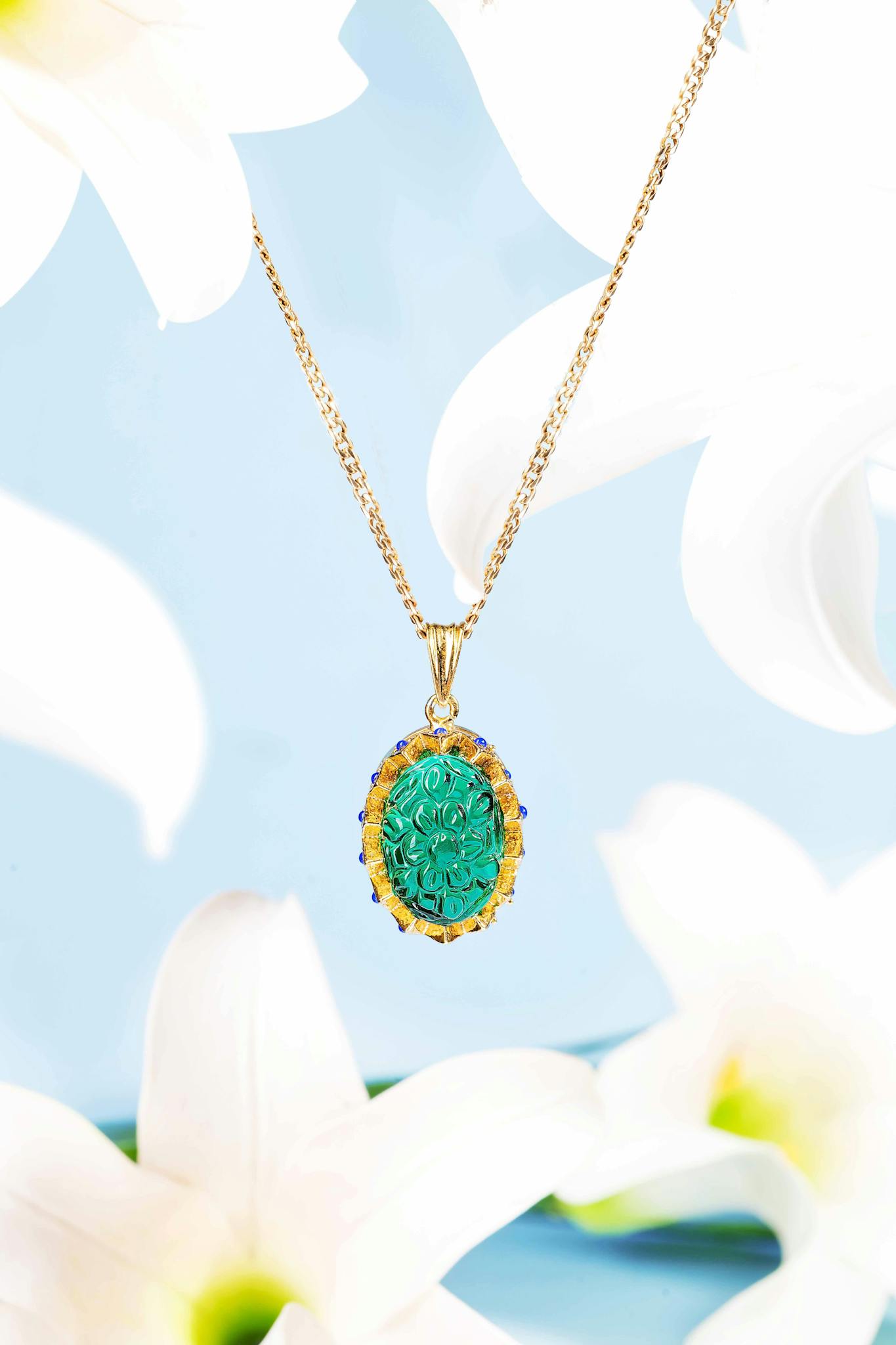 Intricate gold pendant featuring a turquoise gemstone amidst white lilies on a blue background.
